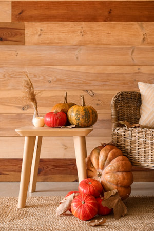Vase with pampas grass, pumpkins and fallen leaves on table near wooden wallの写真素材