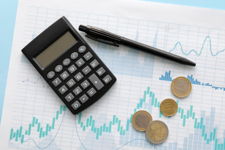 Calculator with pen, coins and diagrams on blue background. Exchange rate conceptの写真素材