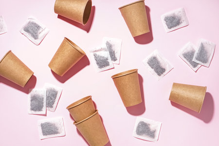 Paper cups and tea bags on pink background