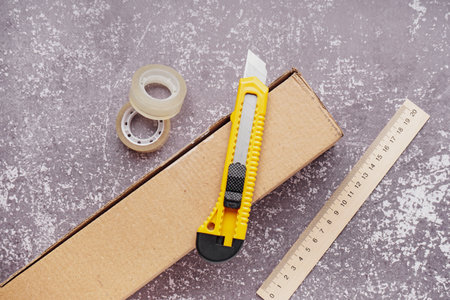Utility knife with box, ruler and adhesive tapes on grunge background