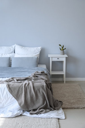 Table with houseplant and big bed near gray wallの写真素材