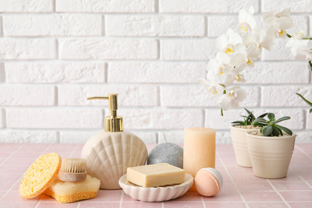 Set of bath supplies with houseplants on table near light brick wall