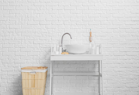 Modern sink and laundry basket near white brick wall