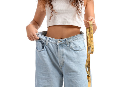 Young African-American woman in loose clothes and with measuring tape on white background. Diet conceptの写真素材