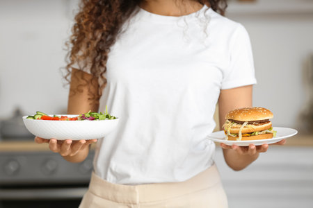 Young African-American woman with healthy and unhealthy food in the kitchen. Diet conceptの写真素材