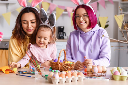 Young lesbian couple with little daughter during painting of Easter eggs in kitchenの写真素材