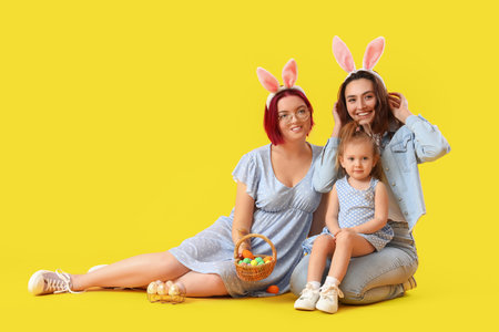 Happy lesbian couple with little daughter and Easter eggs on color backgroundの写真素材