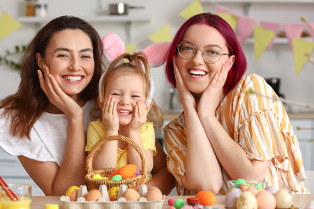 Young lesbian couple with little daughter during painting of Easter eggs in kitchenの写真素材