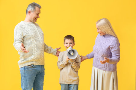Little boy with megaphone and his grandparents in warm sweaters on yellow backgroundの写真素材