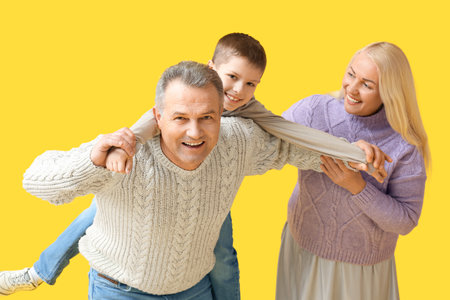 Little boy with his grandparents in warm sweaters having fun on yellow background