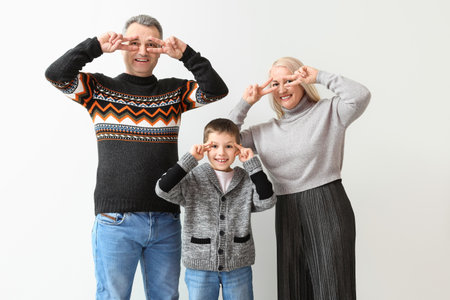 Little boy with his grandparents in warm sweaters dancing on light backgroundの写真素材
