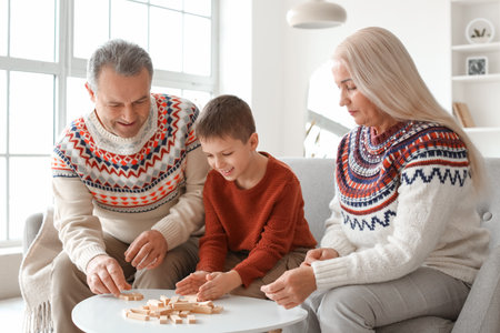 Little boy with his grandparents in warm sweaters playing jenga game at homeの写真素材