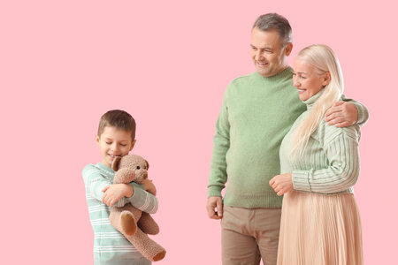Little boy with toy and his grandparents in warm sweaters on pink backgroundの写真素材
