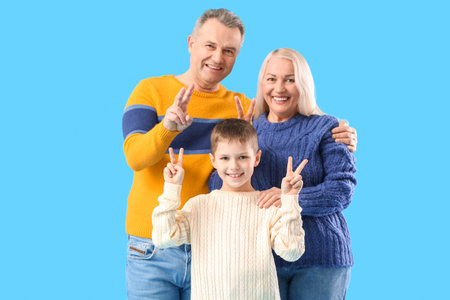 Little boy with his grandparents in warm sweaters showing victory gesture on blue background