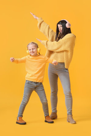 Little girl and her mother in headphones and warm sweaters dancing on yellow backgroundの写真素材