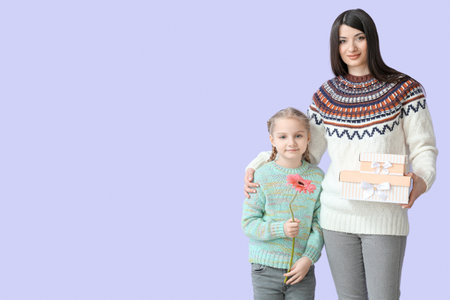 Little girl and her mother in warm sweaters with presents on lilac backgroundの写真素材