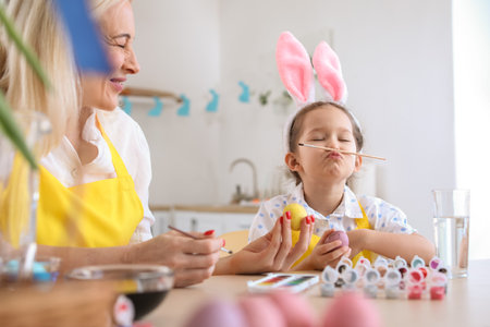 Little girl having fun with her grandmother while painting Easter eggs at homeの写真素材