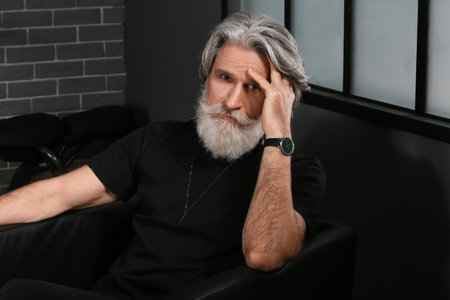 Portrait of handsome mature bearded man sitting in armchair at home