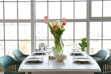 Dining table with beautiful setting and tulips for International Women's Day celebration near window