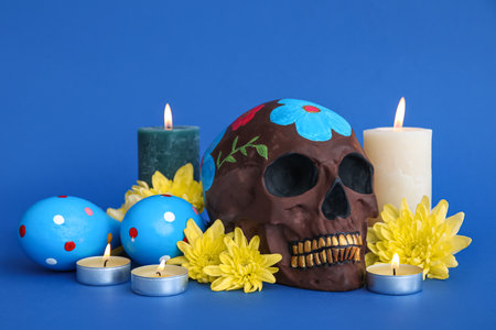 Painted skull for Mexico's Day of the Dead (El Dia de Muertos), flowers and burning candles on blue backgroundの写真素材