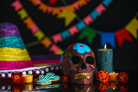 Painted human skull with marigold flowers, cookies and burning candles on dark background. El Dia de...