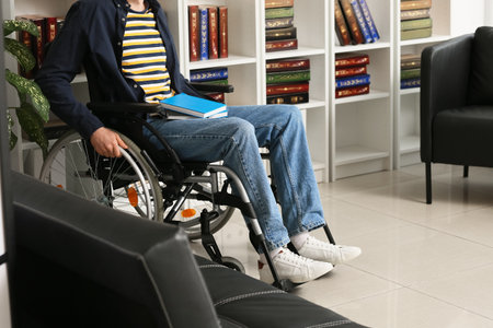Young man in wheelchair choosing book in home libraryの写真素材