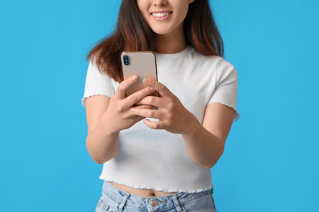 Beautiful young Asian woman with mobile phone on blue backgroundの写真素材