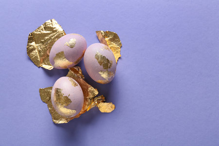 Beautiful Easter eggs and golden foil on lilac backgroundの写真素材