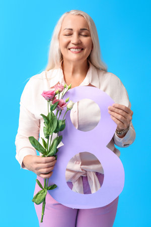 Mature woman holding eustoma flowers and paper figure eight on blue background. International...