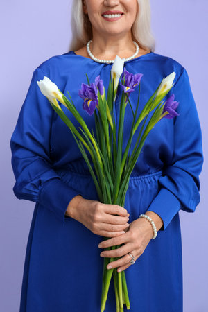 Mature woman with bouquet of iris flowers on violet background. International Women's Day celebrationの写真素材