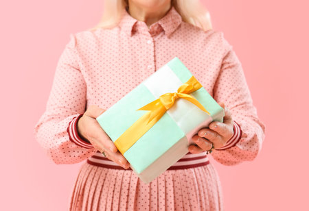Beautiful mature woman holding gift box on pink background, closeup. International Women's Day celebrationの写真素材