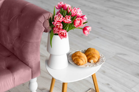 Vase with tulip flowers and plate with croissants on coffee table in living room, closeupの写真素材