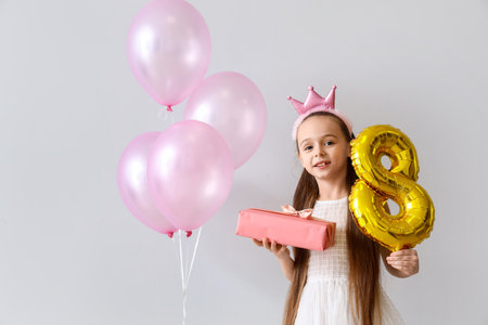 Cute little girl with gift and balloons on light background. International Women's Day celebration