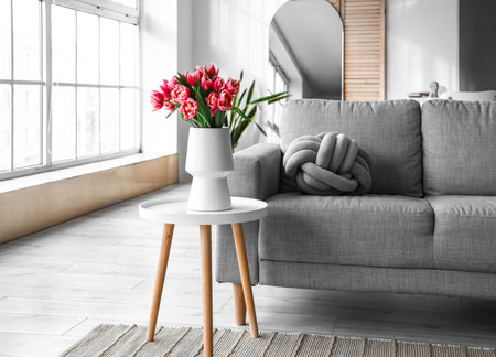 Vase with tulip flowers on small table and sofa in living roomの写真素材