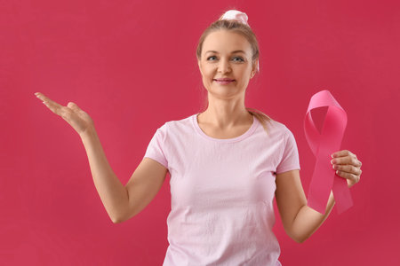 Woman holding pink awareness ribbon and pointing at something on red background. breast cancer awareness conceptの写真素材