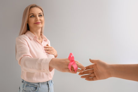 Woman with pink awareness ribbon shaking hands on light background. breast cancer awareness conceptの写真素材