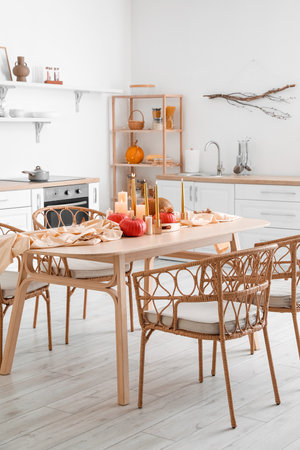 Dining table with pumpkins, fallen leaves and burning candles in light kitchenの写真素材