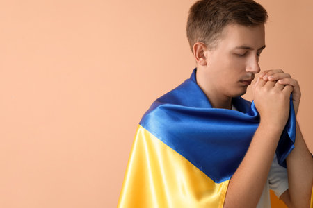 Young man with flag of Ukraine praying on beige backgroundの写真素材