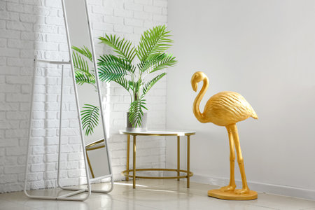 Golden flamingo, mirror and table with houseplant near white wall in roomの写真素材
