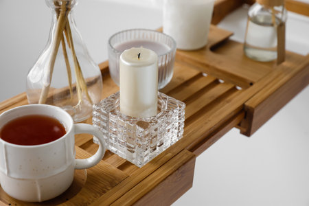 Holder with candle and cup of tea on wooden bathtub trayの写真素材