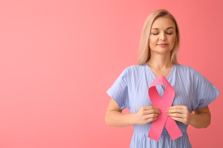 Woman with closed eyes holding pink awareness ribbon on color background. breast cancer awareness conceptの写真素材