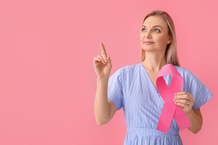 Woman holding pink awareness ribbon and pointing at something on color background. breast cancer awareness conceptの写真素材