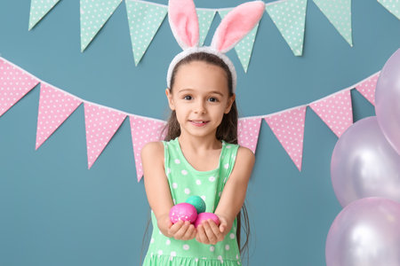 Little girl with bunny ears holding Easter eggs on blue backgroundの写真素材