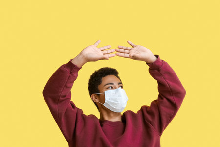 Young African-American man in medical mask protecting himself on yellow background. immunity conceptの写真素材