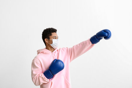 Young African-American man in medical mask with boxing gloves on white background. immunity concept
