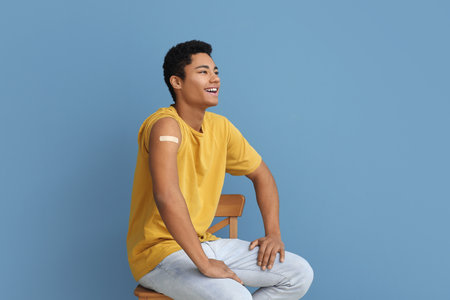 Young African-American man with applied medical patch sitting in chair on blue backgroundの写真素材