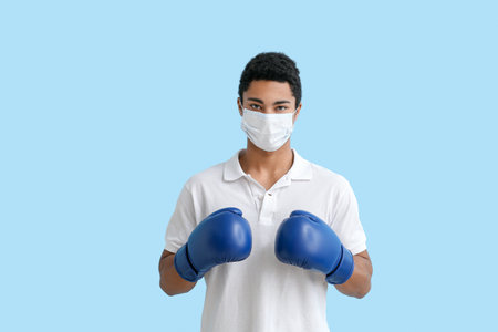 Young African-American man in medical mask with boxing gloves on blue background. immunity conceptの写真素材
