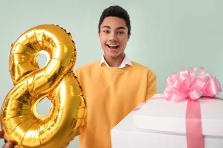 African-American man with gift boxes and balloon in shape of figure 8 on light background....
