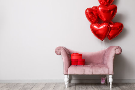 Beautiful heart-shaped balloons for Valentine's Day celebration and sofa near light wall in roomの写真素材