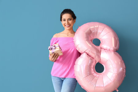 Woman with gift and balloon in shape of figure 8 on color background. International Women's Day...